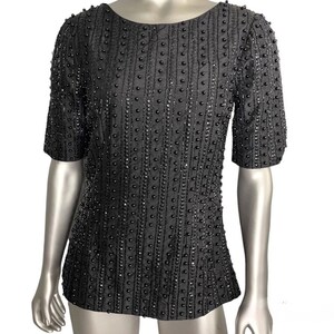 May include: A black beaded top with a round neckline and short sleeves. The top is covered in small black beads that create a textured pattern.