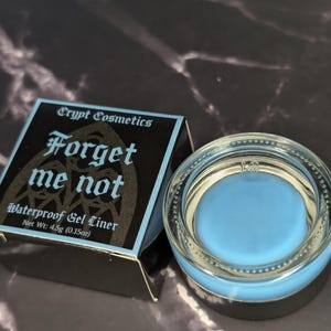 May include: A light blue waterproof gel eyeliner by Crypt Cosmetics. The product is in a clear glass jar with a silver rim, next to a black and light blue box with the text "Forget me not". The net weight is 4.5g (0.15oz).