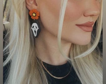 Può includere: Un paio di orecchini pendenti con un ciondolo a forma di fantasma bianco e nero e un ciondolo a forma di fiore arancione brillante.