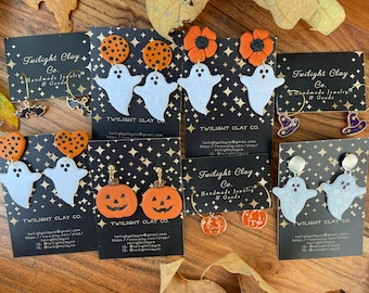 May include: Assortment of Halloween-themed polymer clay earrings.  The earrings feature ghosts, pumpkins, and candy corn.  The earrings are displayed on black cards with the text "Twilight Clay Co. Handmade Jewelry & Goods" and contact information.