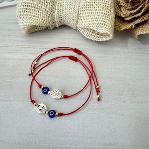 May include: Two red string bracelets with blue evil eye charms and silver charms. One charm features a hand with an inscription and the other charm features a circle with an inscription.