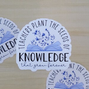 May include: Two white stickers with blue accents feature an open book with flowers and the text "Teachers plant the seeds of knowledge that grow forever".