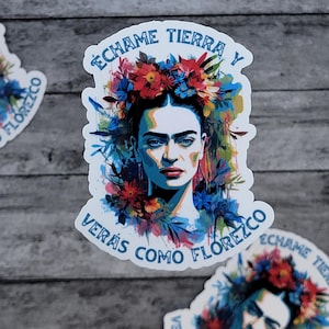 May include: A colorful sticker featuring a portrait of Frida Kahlo with a floral crown. The sticker has the text "Échame tierra y verás como florezco" in Spanish, which translates to "Throw me dirt and you will see how I bloom."