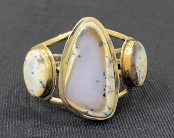 Peut inclure: Bracelet manchette doré avec trois pierres ovales et en forme de goutte. Les pierres présentent un motif crème, gris et marron. Le bracelet a un design ouvert unique.