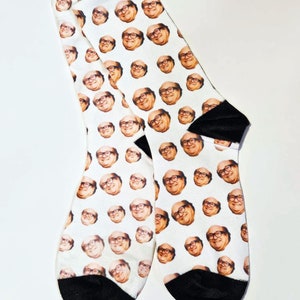 May include: A pair of white socks with a repeating pattern of a man's face. The socks have black toes and heels.