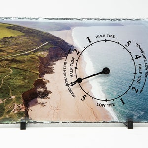 May include: A slate tide clock featuring a coastal scene. The clock face displays the hours until high tide and low tide. The clock hand is pointing to the 4 hour mark, indicating that it is 4 hours until low tide.