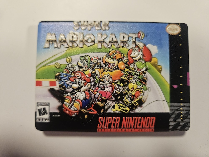 Puede incluir: Un cartucho de videojuego Super Mario Kart. El cartucho presenta una colorida ilustraci&oacute;n de Mario y otros personajes corriendo en una pista. Las palabras "SUPER MARIO KART" y "SUPER NINTENDO" se muestran de forma destacada.