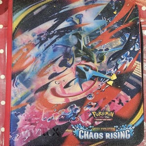 May include: A red-edged card binder featuring a vibrant, abstract design with blue, red, and yellow accents. The cover displays the "Pokemon Trading Card Game" logo and the text "Mega Evolution Chaos Rising".