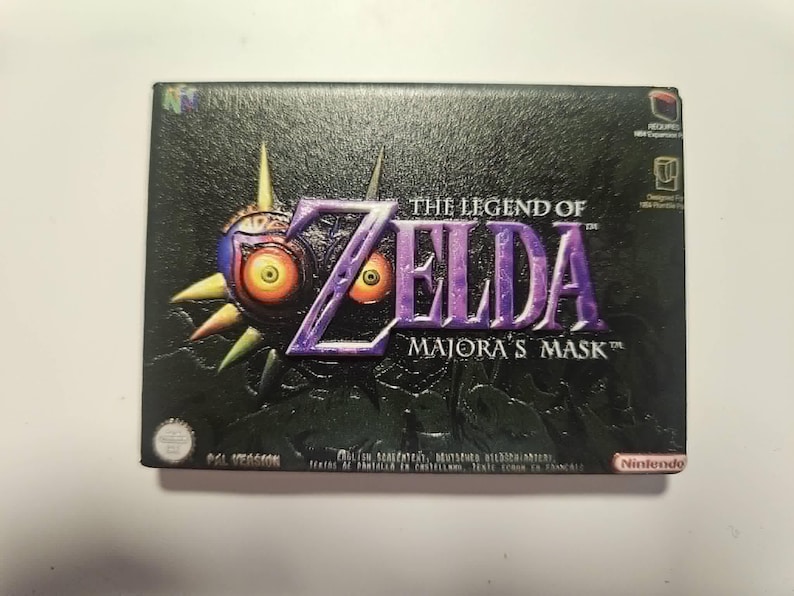 Op de afbeelding: Gamebox van The Legend of Zelda: Majora's Mask. De doos is zwart met de speltitel in paars en het iconische masker met gele ogen. Het Nintendo-logo staat rechtsonder.