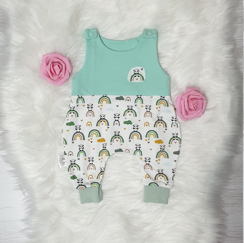 May include: A light blue and white baby romper with a panda bear and rainbow print. The romper has a sleeveless top and a pocket on the front.