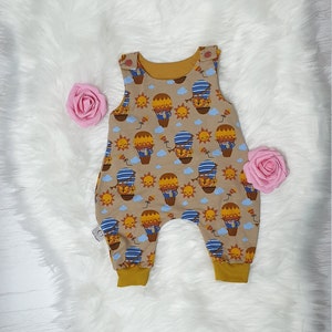 May include: A brown and yellow baby onesie with a hot air balloon print. The onesie has a mustard yellow trim around the neck and leg openings.