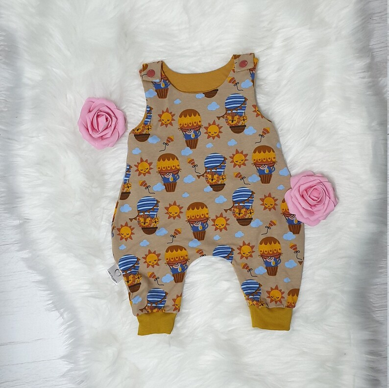 May include: A brown and yellow baby onesie with a hot air balloon print. The onesie has a mustard yellow trim around the neck and leg openings.
