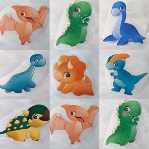 Könnte beinhalten: Neun bunte Dinosaurier-Aufkleber. Die Aufkleber zeigen verschiedene Dinosaurier in Orange-, Grün- und Blautönen. Zu den Dinosauriern gehören ein Pterodactylus, ein Triceratops und ein Brontosaurus. Die Aufkleber befinden sich auf weißem Hintergrund.