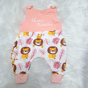 May include: A pink and white baby onesie with a lion print. The onesie has a pink top with the text "kleines Wunder" in white.