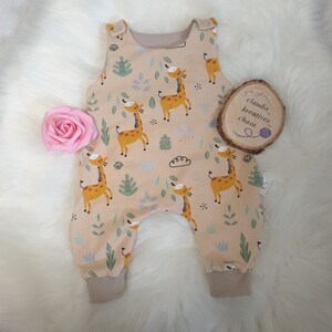 May include: A beige baby onesie with a pattern of giraffes and leaves. The onesie has adjustable straps and a snap closure. The onesie is made of soft, comfortable fabric.