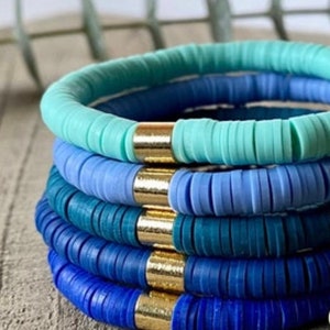 May include: Stack of five bracelets made of blue and turquoise colored beads with gold accents.