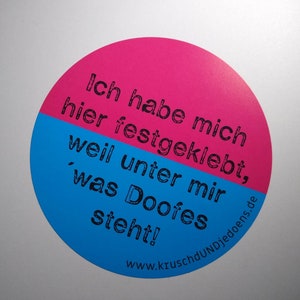Könnte beinhalten: Ein runder Aufkleber, diagonal in zwei Bereiche unterteilt, rosa und blau. Der rosafarbene Bereich enthält deutschen Text, während der blaue Bereich ebenfalls deutschen Text und eine Website-Adresse unten enthält.