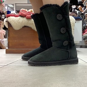 May include: Black suede knee-high boots with a faux fur trim and three large buttons on the shaft.