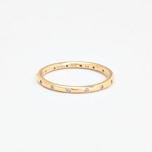 May include: A thin gold band ring featuring evenly spaced, small, clear, round-cut stones set flush into the metal. The interior of the band is clearly engraved with the text G585, ALE, and the number 54, indicating the ring size and metal purity.