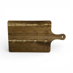 Peut inclure: Planche de service rectangulaire en bois avec une poignée et 16 creux circulaires. La planche est en bois brun clair avec un grain visible et une finition lisse. La poignée comporte un trou pour suspendre.