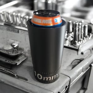 Puede incluir: Un vaso negro con el texto "10mm" en blanco, que sostiene una lata naranja y azul. La lata tiene las palabras "MENTAL FOCUS" impresas. El vaso está sobre una superficie metálica.