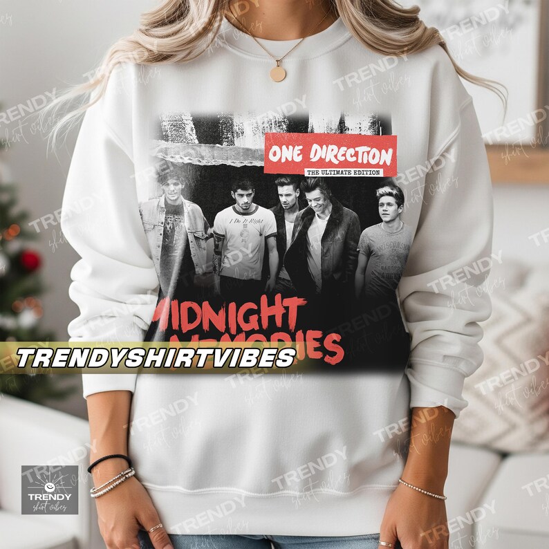 A person wearing a white sweatshirt with a black and white image of the members of the popular music group One Direction, along with the text "Midnight Vibes" and "One Direction" printed on it.
