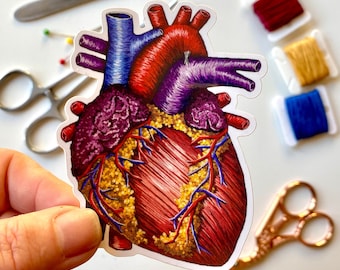 以下が含まれることがあります： カラフルな刺繍が施された解剖学的心臓のステッカーのクローズアップ。心臓は赤、紫、青で、金色のアクセントが付けられています。ステッカーは白い背景の上にあります。