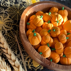 May include: A wooden bowl filled with small orange pumpkins. The pumpkins are all about the same size and have green stems. The bowl is sitting on a black fabric with a gold design.