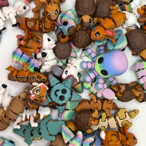 May include: A selection of colourful, articulated animal figurines. The collection includes sheep, turtles, rabbits, and an octopus, with rainbow and pastel colour schemes. The toys are made of plastic and have a segmented design, allowing for movement.