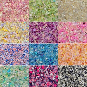 May include: A collection of twelve distinct square panels displaying assorted craft embellishments, including miniature resin flowers, beads, sequins, and charms in various color palettes such as pink, green, blue, purple, yellow, and monochrome.