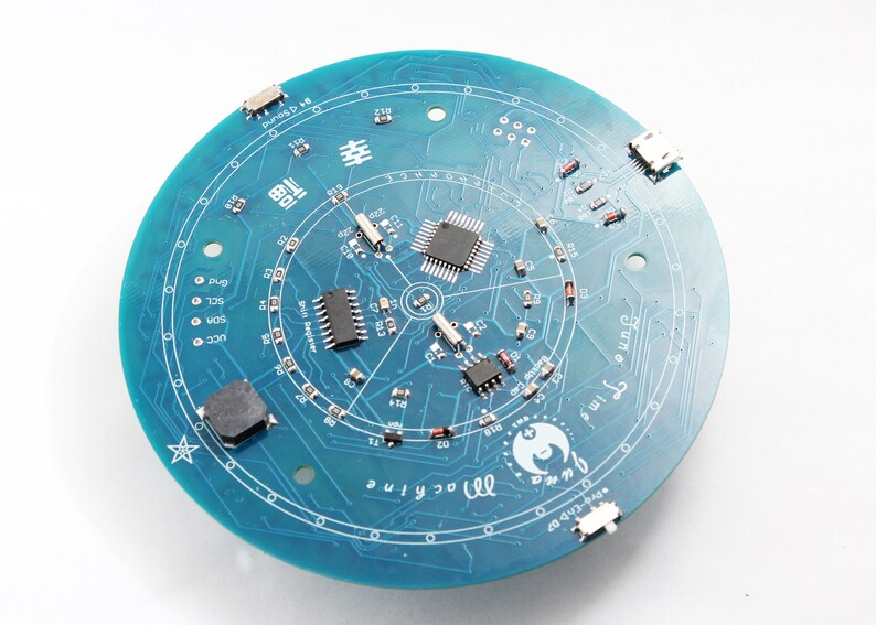May include: A circular teal circuit board with various electronic components, including chips, resistors, and connectors. The board features intricate circuit patterns and text, including "June", "machine", and "Pro-CAD".