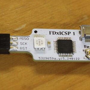 May include: A white circuit board with a black chip, a small LED, and a micro USB connector. The board is labelled "FDxICSP 1" and has a reset button.