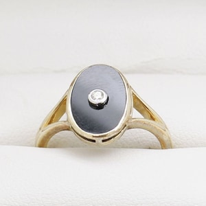 May include: A gold ring with a black oval stone set in the center. A small diamond is set in the stone.