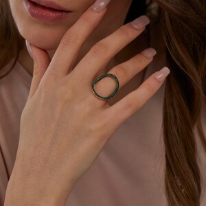 Puede incluir: Un anillo de oro con una piedra ovalada verde engastada en el centro. El anillo está en el dedo de una persona.