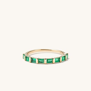 May include: A gold band ring with a row of emerald green baguette-shaped stones.
