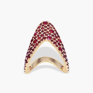 Op de afbeelding: Een V-vormige ring van geelgoud met een puntig ontwerp dat volledig is ingelegd met talloze kleine, ronde, dieprode robijnen. De ringband heeft een gladde, gepolijste gouden binnenzijde die contrasteert met de textuur van de met stenen bezette buitenkant.