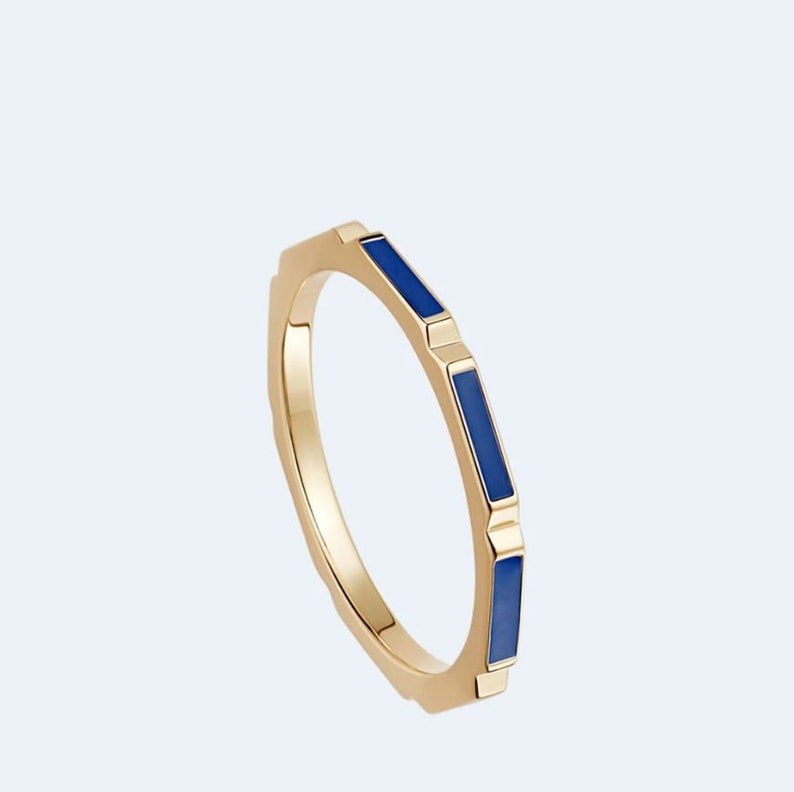 May include: A gold ring with blue enamel accents. The ring has a geometric design and is a simple, elegant piece of jewellery.