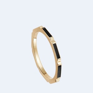 May include: A gold ring with black enamel accents. The ring has a geometric shape and is a simple, elegant design.