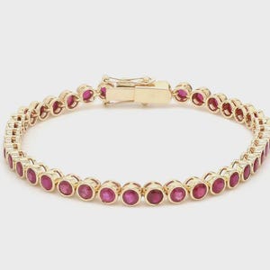 Puede incluir: Un brazalete dorado con una serie de piedras preciosas redondas de color rojo brillante. El brazalete tiene un cierre seguro. Las piedras están espaciadas uniformemente y engastadas en biseles individuales. El diseño es clásico y elegante.