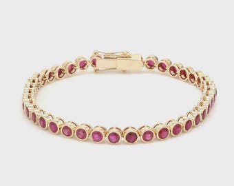 May include: A gold-colored bracelet featuring a series of round, vibrant red gemstones. The bracelet has a secure clasp and is designed with a classic, elegant style. The gemstones are evenly spaced and set in individual bezels.