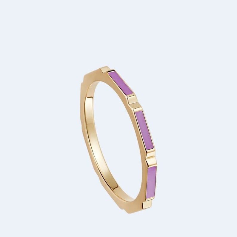 May include: A gold ring with a geometric design and purple enamel accents.