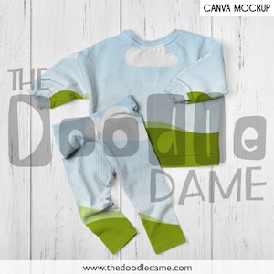 May include: A light blue sweatshirt and matching leggings with a green and white landscape design. The text "The Doodle Dame" is printed on the clothing.