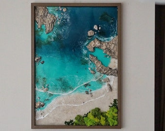 May include: A framed artwork depicting a beach scene with turquoise water, white sand, and green foliage. The artwork is in a brown frame and appears to be a 3D mixed media piece.