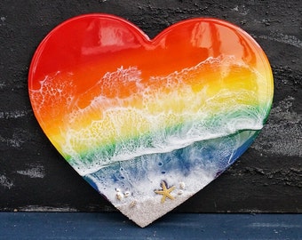 May include: A heart-shaped resin art piece with a rainbow wave design and white foam. The bottom of the piece is decorated with seashells and a starfish.