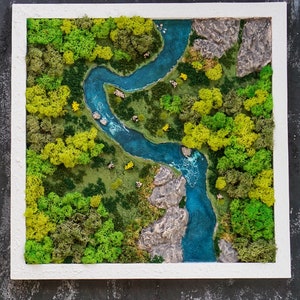 Puede incluir: Una pieza de arte de musgo enmarcada que representa un r&iacute;o serpenteando a trav&eacute;s de un bosque verde. El r&iacute;o es de un azul vibrante y el bosque est&aacute; hecho de musgo preservado en tonos verdes y amarillos.