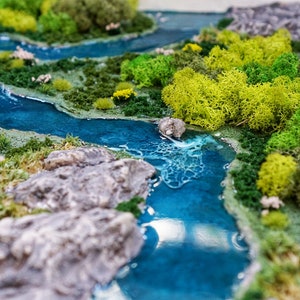Puede incluir: Un paisaje en miniatura con un r&iacute;o de resina azul serpenteando a trav&eacute;s de musgo verde y rocas grises.