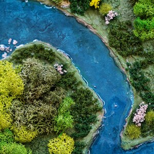 Puede incluir: Una escena de paisaje en miniatura con un r&iacute;o azul serpenteando a trav&eacute;s de un bosque verde y musgoso. El r&iacute;o es de color azul claro y el bosque est&aacute; hecho de musgo preservado.