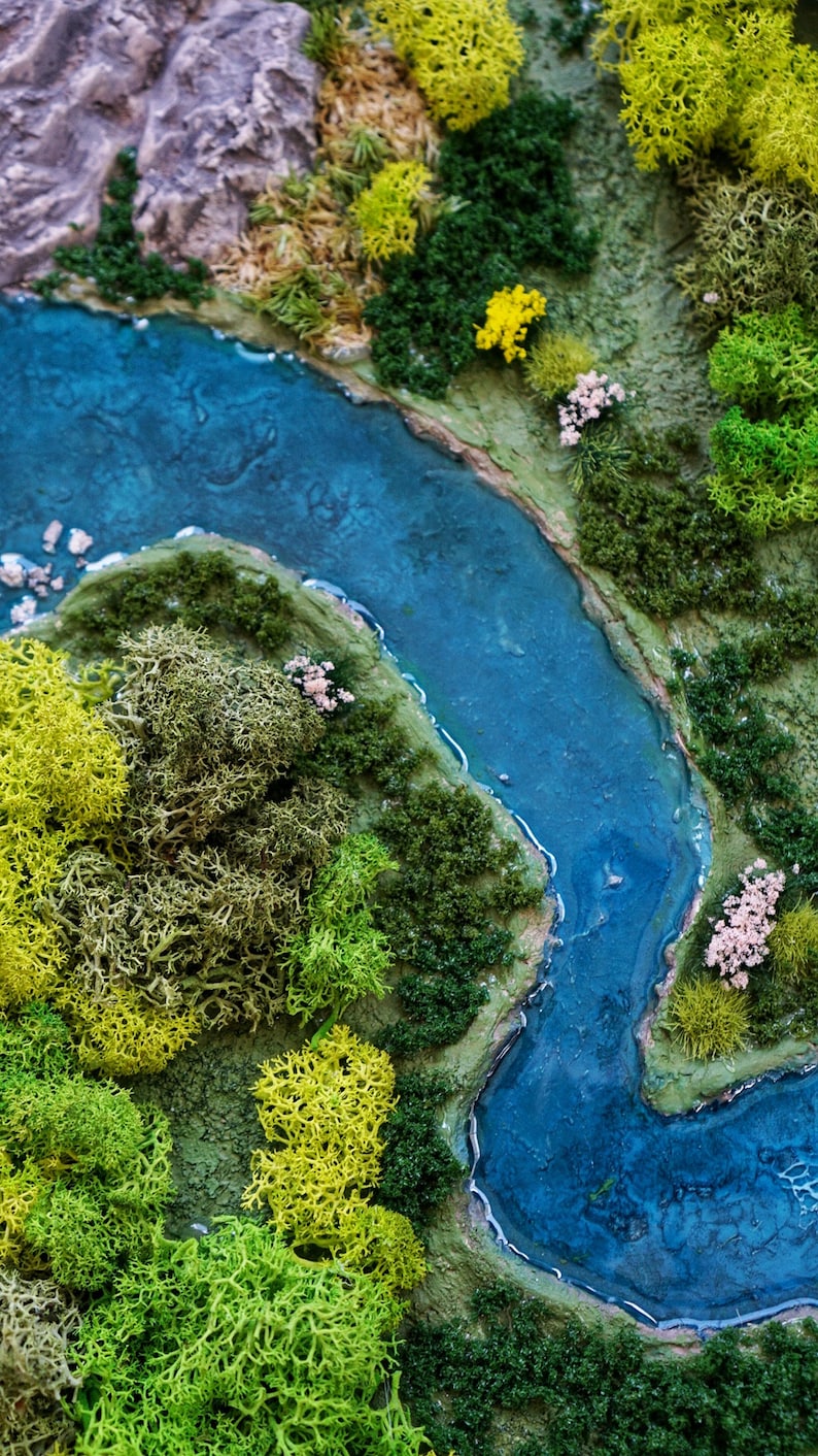 Puede incluir: Una escena de paisaje en miniatura con un r&iacute;o azul serpenteando a trav&eacute;s de un bosque verde y musgoso. El r&iacute;o es de color azul claro y el bosque est&aacute; hecho de musgo preservado.