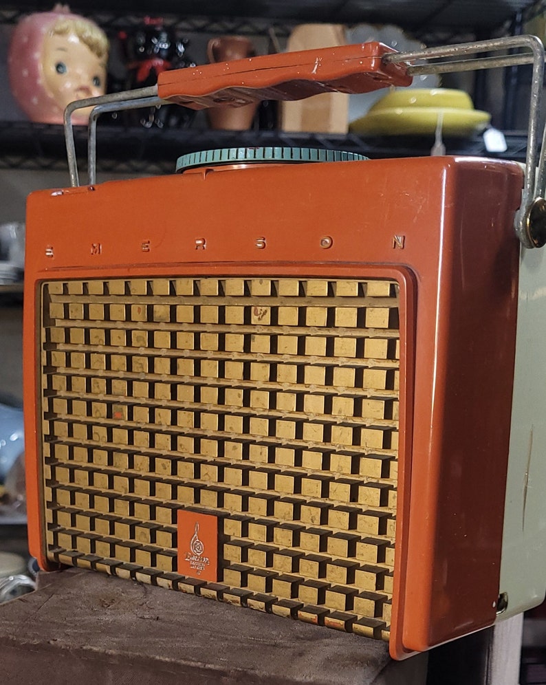 May include: Vintage orange and white Emerson portable radio with a metal carrying handle and a gold speaker grille. The radio has a round dial with a green and white design.