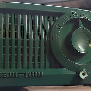 May include: A vintage green Stewart-Warner radio with a round dial and a speaker grille. The dial is marked with numbers from 55 to 160.